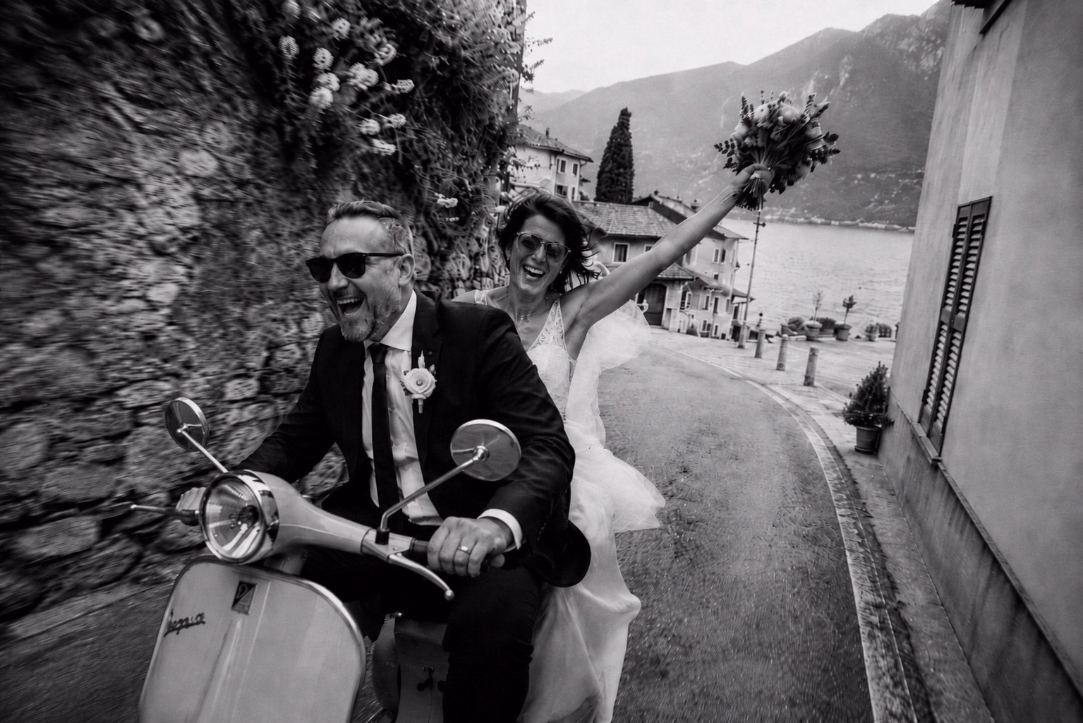 Newlyweds riding a Vespa through a lakeside village