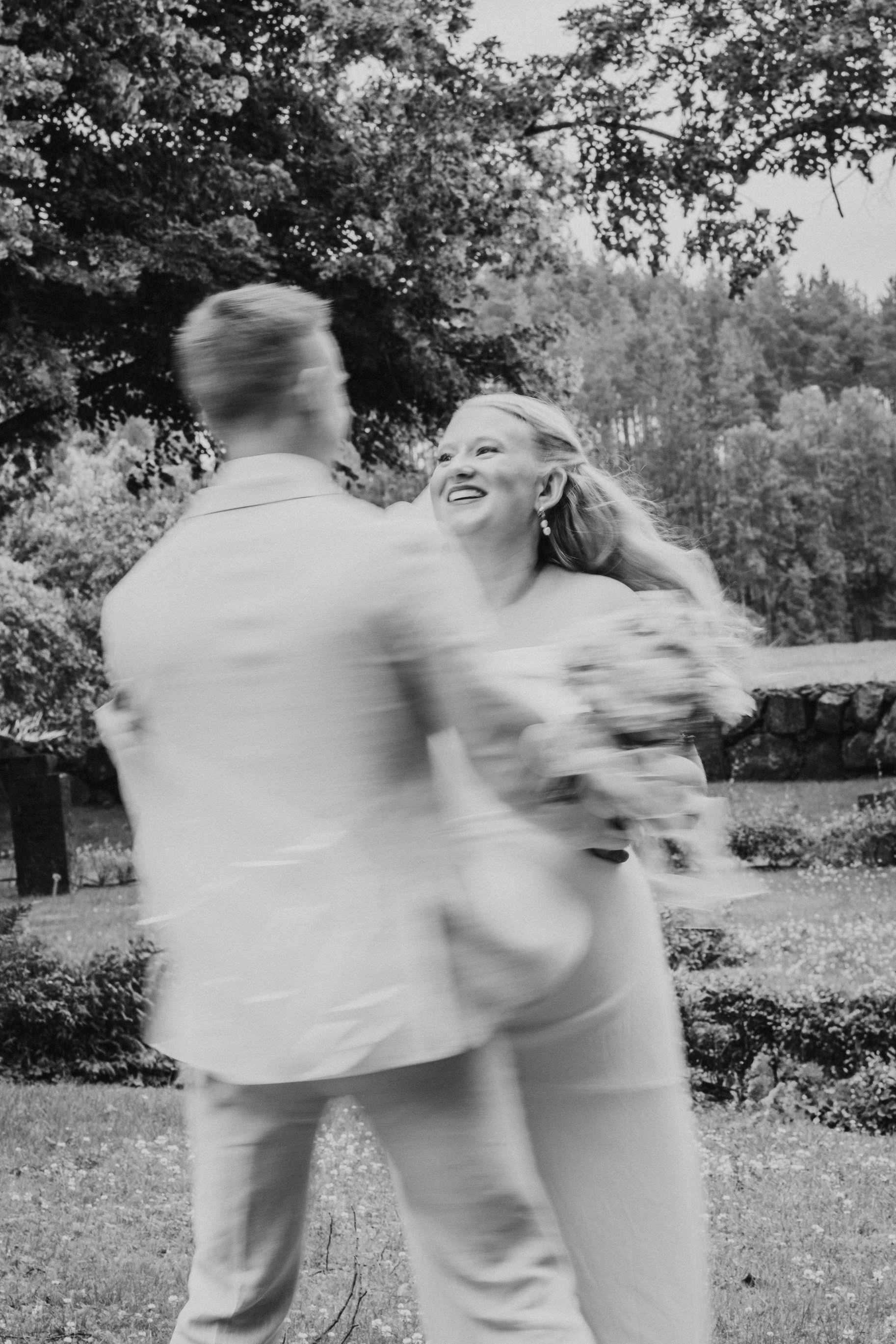 Newlyweds dancing outdoors in a motion-blurred black-and-white photograph