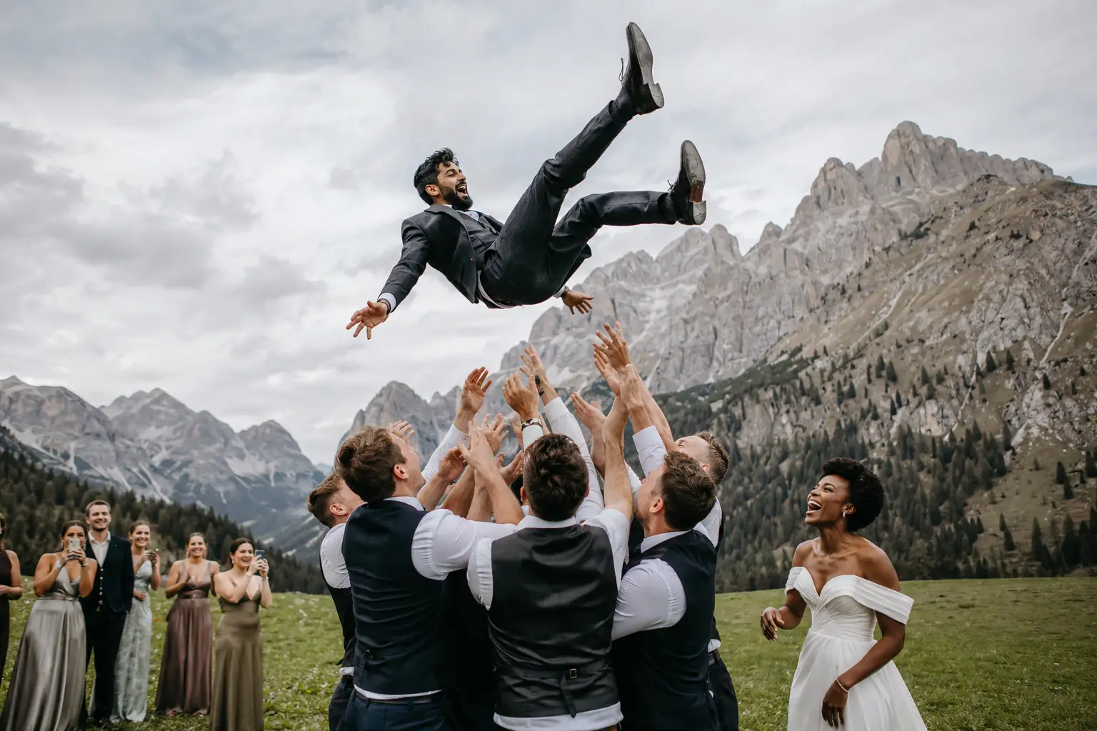 Guests tossing the groom into the air during an outdoor Dolomites wedding, with dramatic alpine peaks creating an unforgettable mountain backdrop.