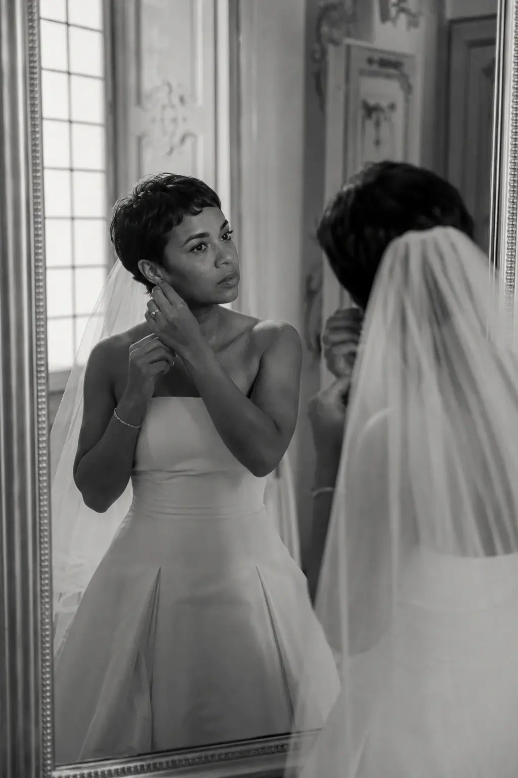 Bride adjusting her earring in front of a mirror during wedding preparations at Villa Sola Cabiati in Lake Como, photographed in a candid black and white documentary style.