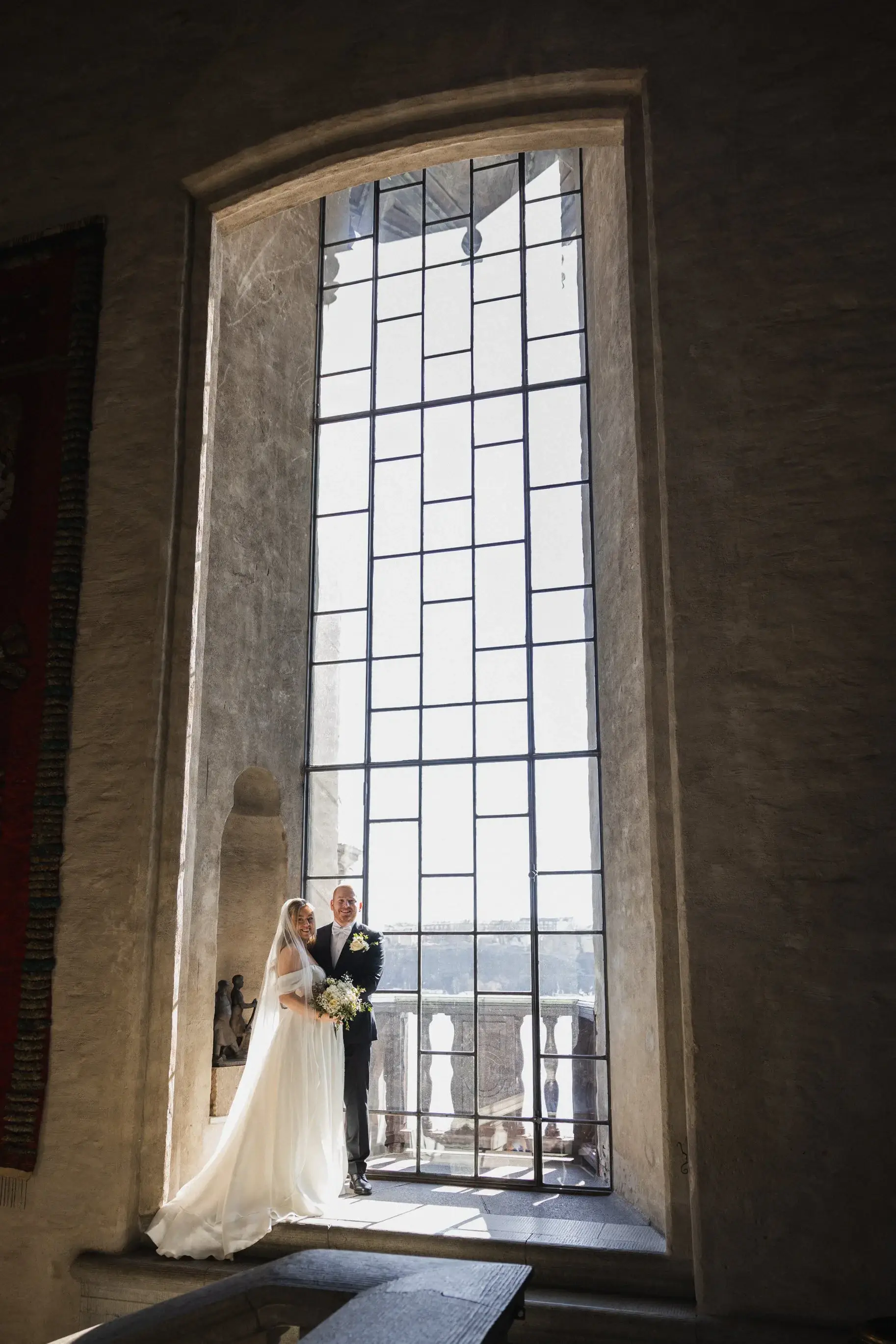 Couple standing beside a tall window at Stockholm City Hall.