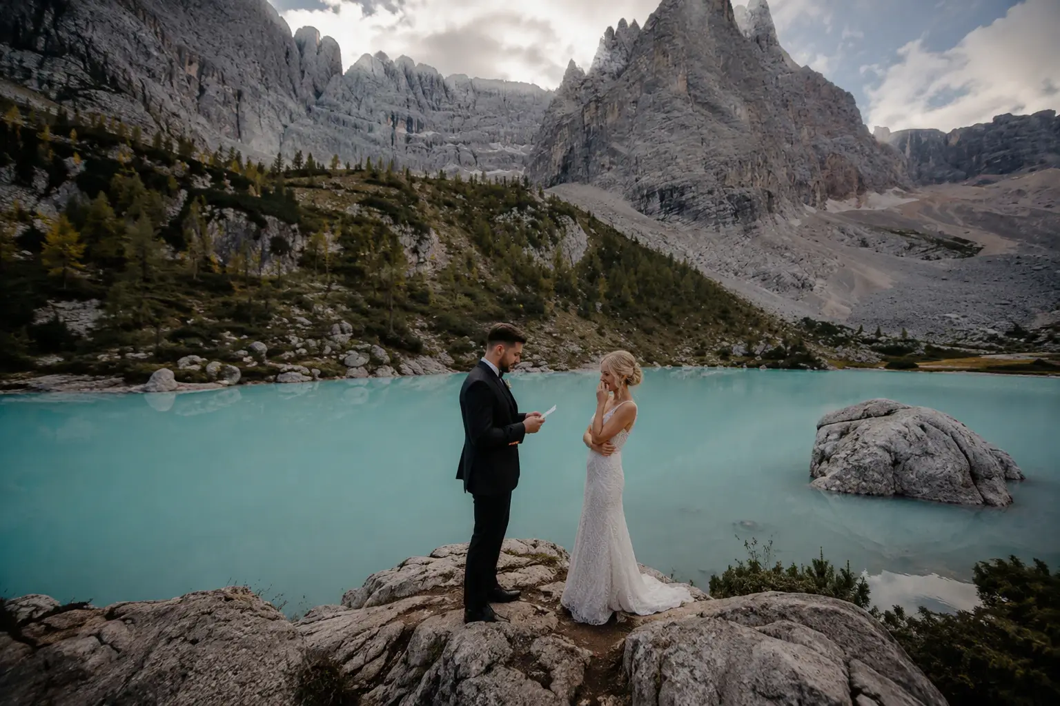 Couple standing on rocks beside a turquoise lake in the Dolomites.