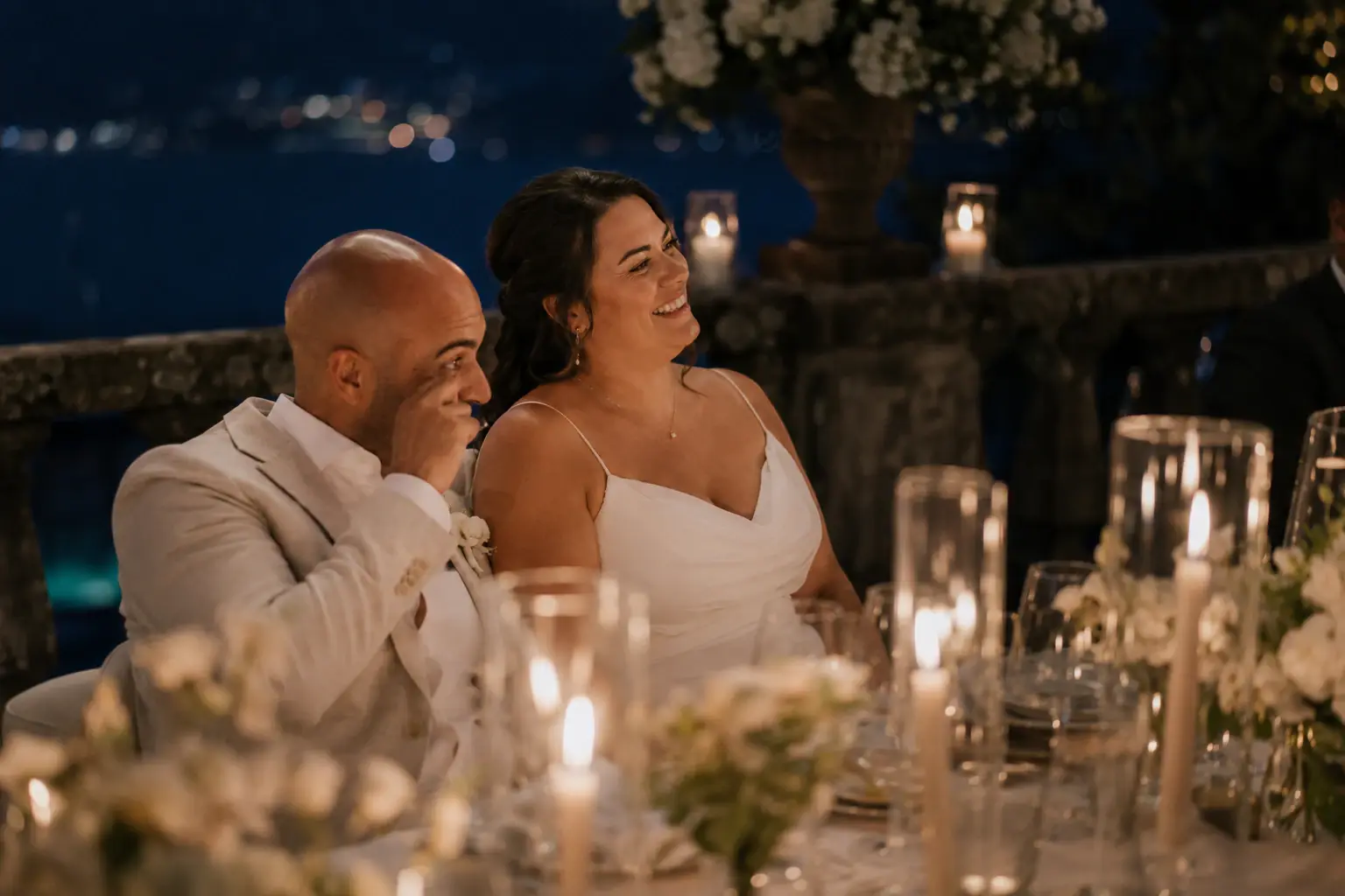 Newlyweds laughing together during an evening wedding dinner.