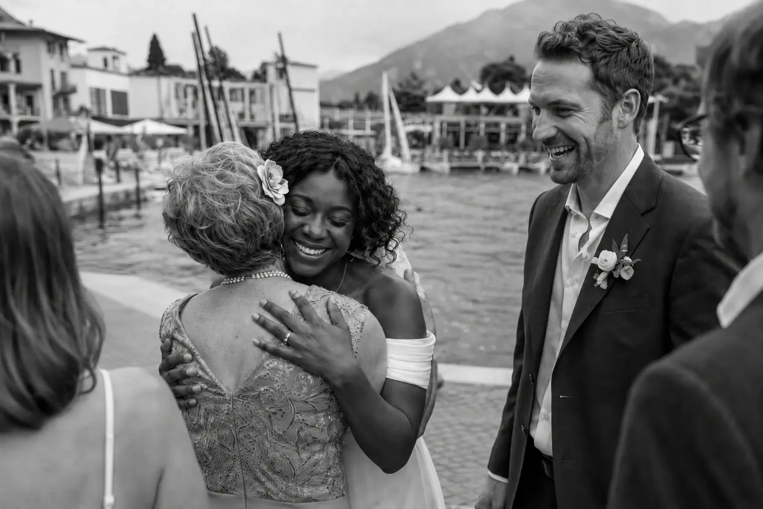 Bride hugging a family member after the ceremony in Riva del Garda while the groom smiles beside Lake Garda in a candid documentary wedding moment.
