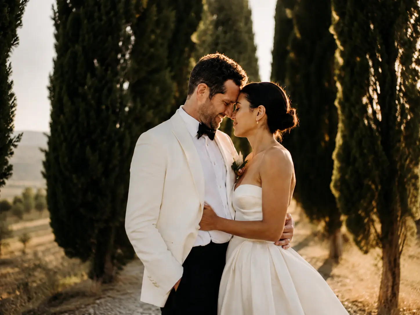 Bride and groom embracing among cypress trees during a destination wedding in Tuscany, Italy, at golden hour.