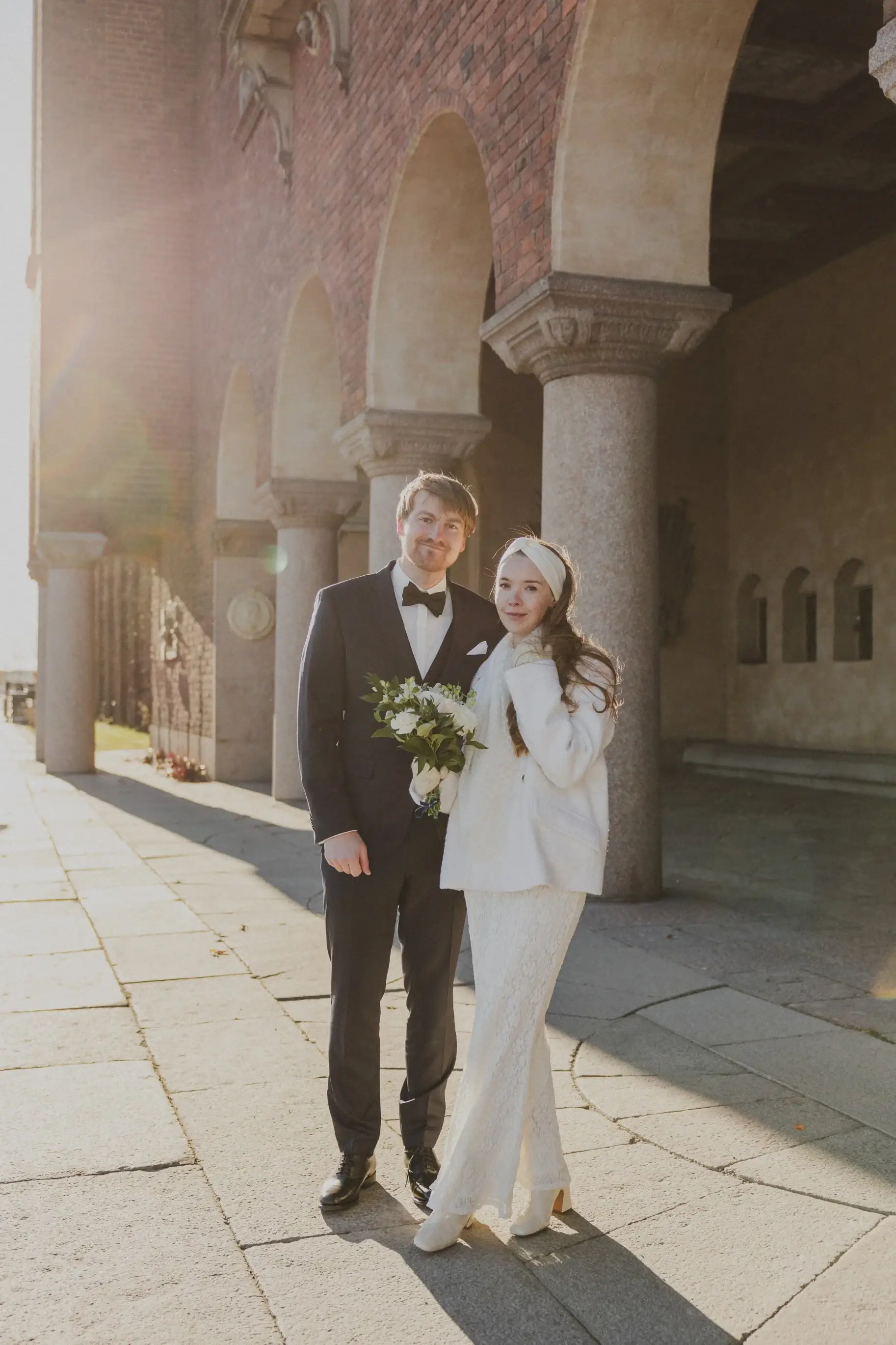 Couple walking through sunlit arches at Stockholm City Hall.