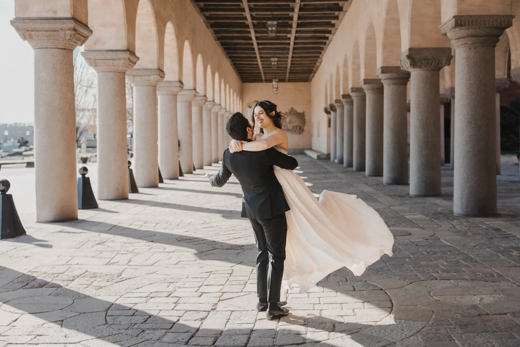 Groom twirling the bride beneath the Stockholm City Hall colonnade.