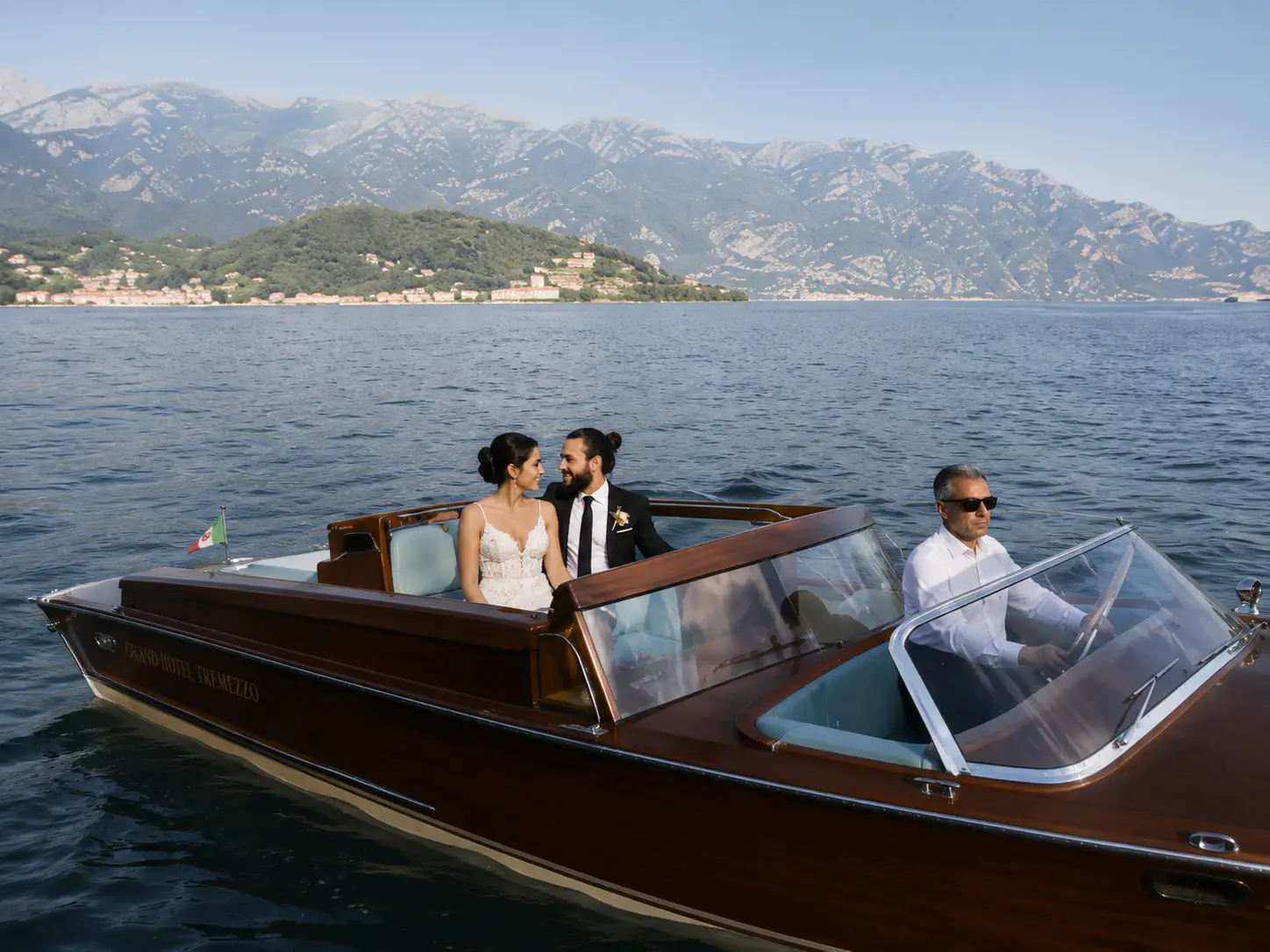 Couple on a classic wooden boat during a Grand Hotel Tremezzo wedding on Lake Como, with cinematic lake views and mountains in the background.