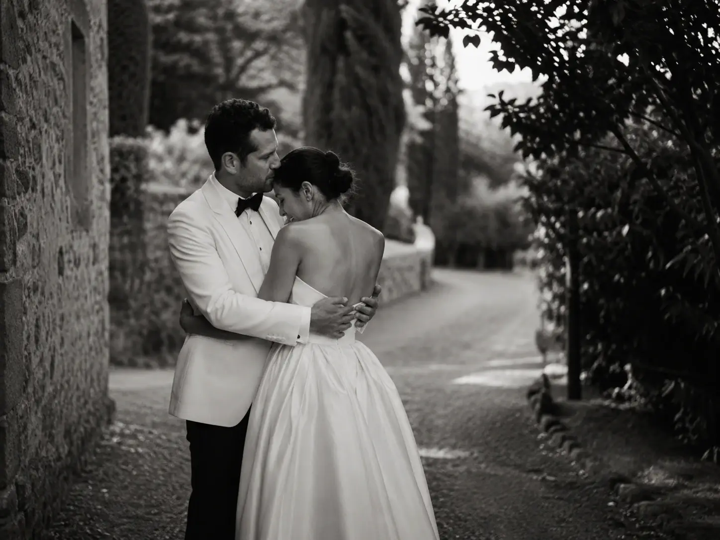 Black and white wedding portrait of a bride and groom embracing on a romantic stone pathway at Borgo Stomennano in Tuscany.