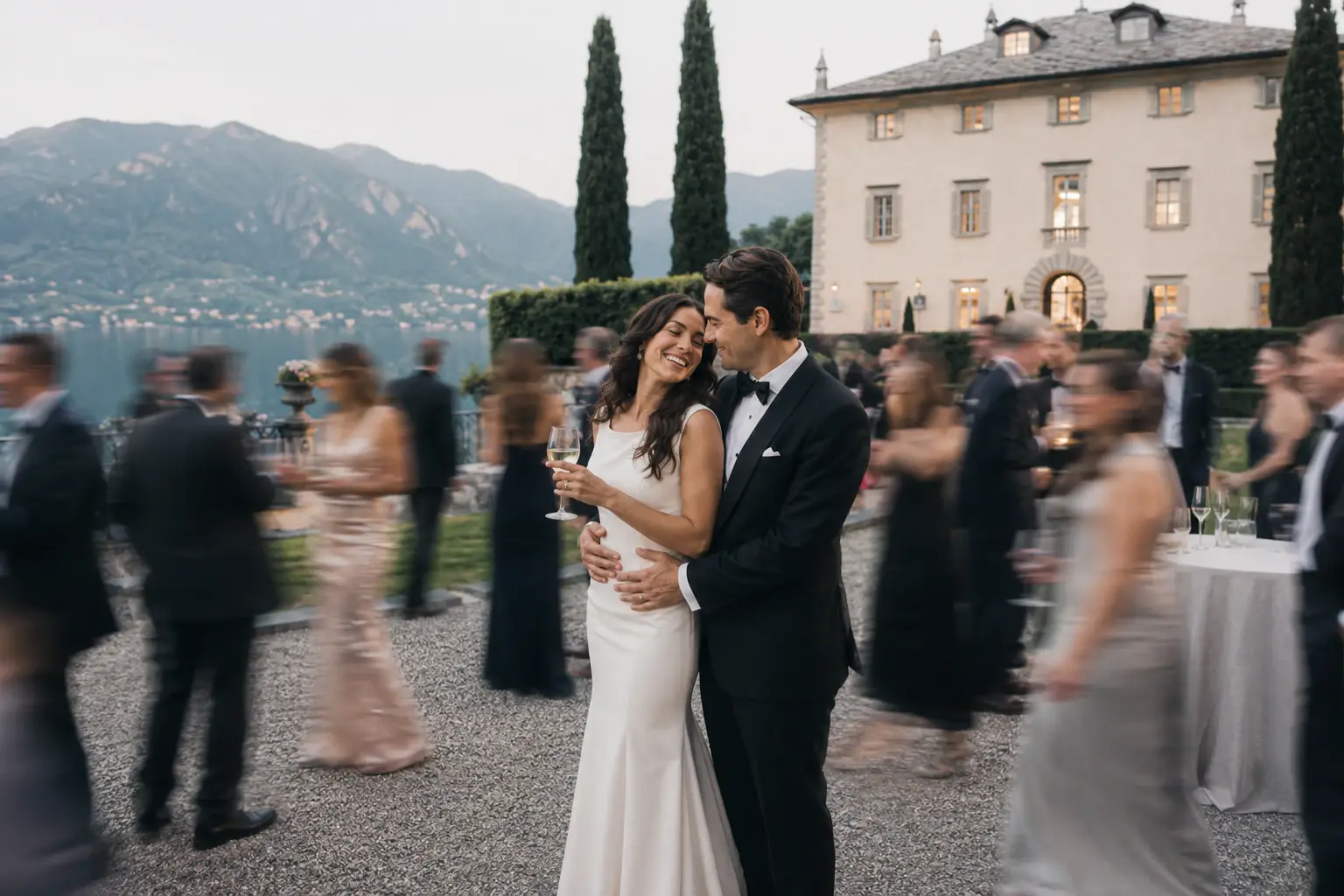 Bride and groom embracing during cocktail hour at Villa Balbiano with cinematic motion blur of wedding guests and Lake Como in the background.