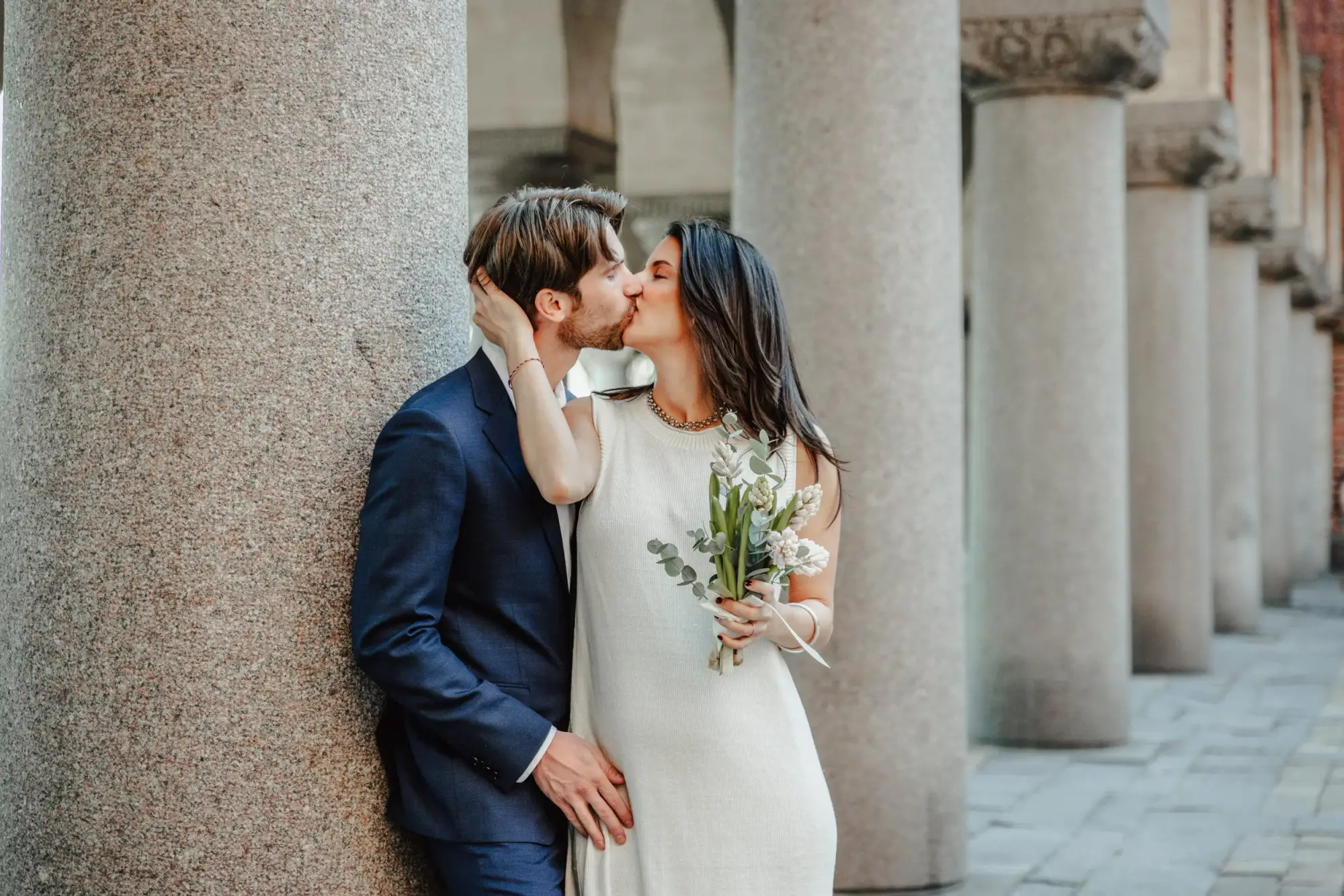 Couple kissing beneath a stone column at Stockholm City Hall.