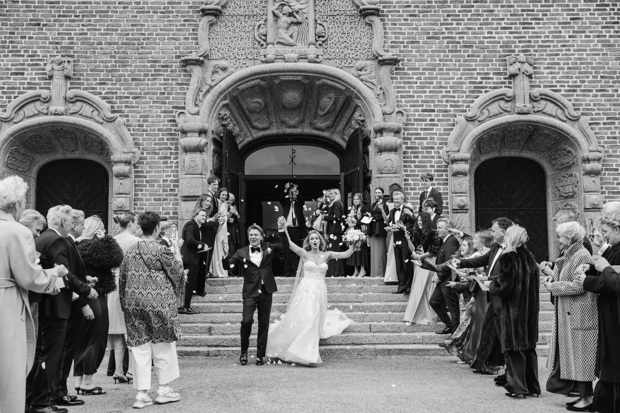 Newlyweds leaving a Stockholm church through rose petals in black and white.