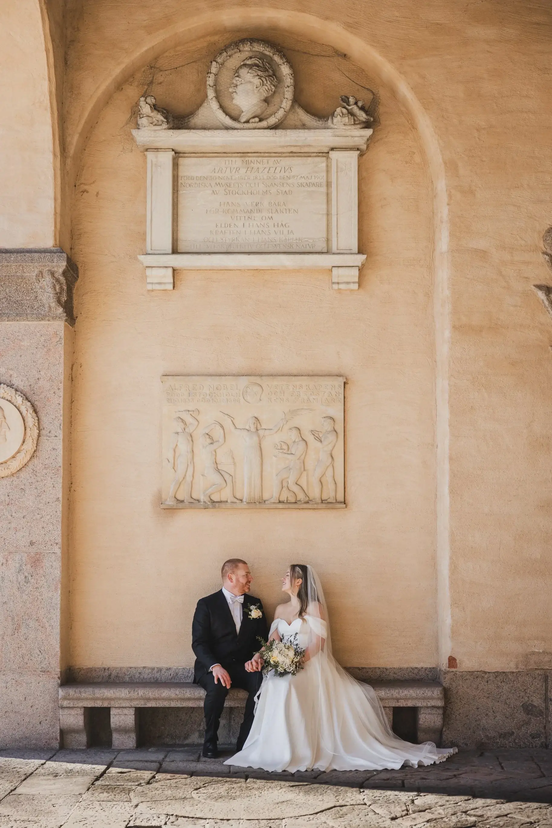 Couple seated together against a stone wall at Stockholm City Hall.