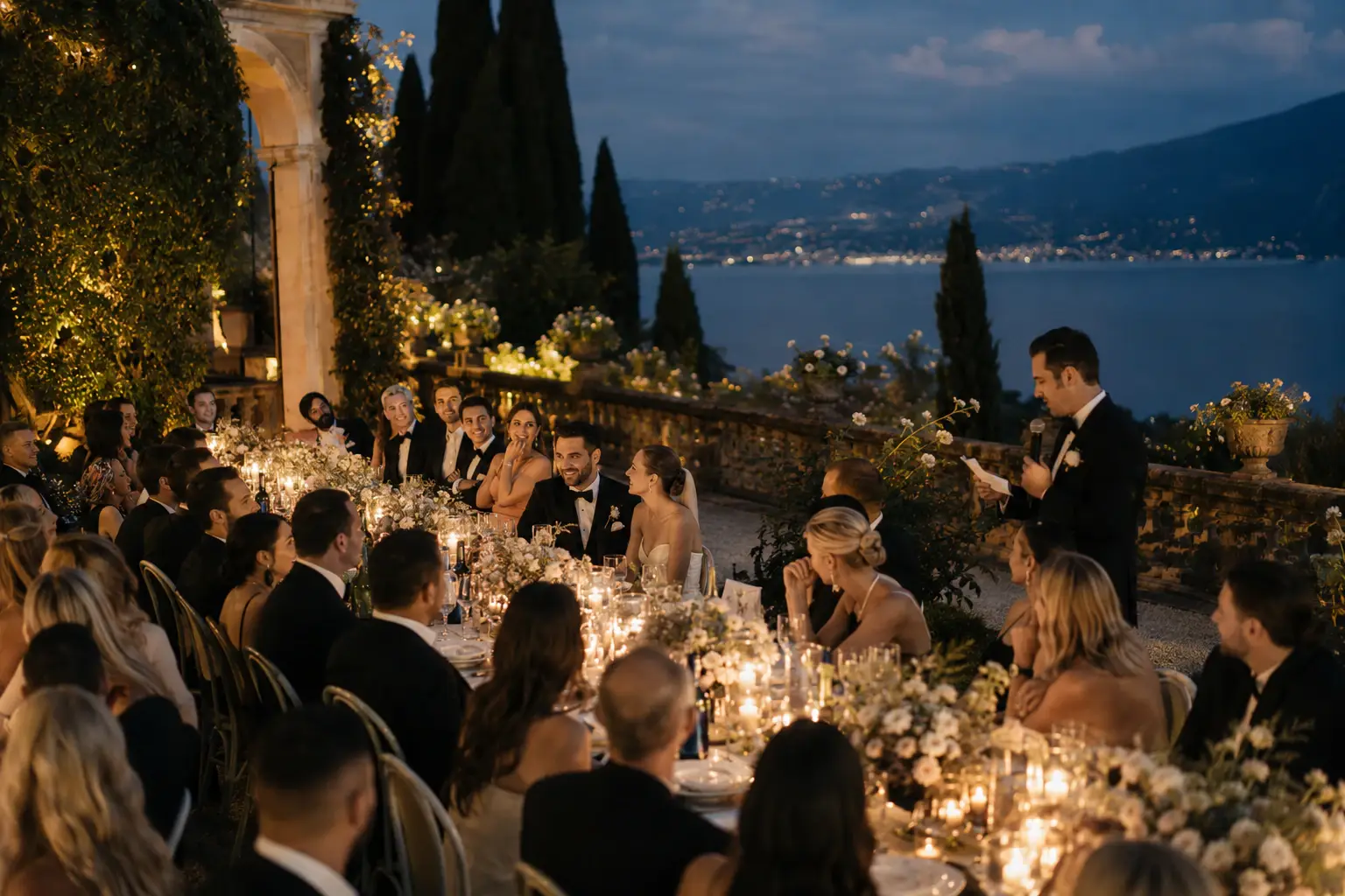 Guests enjoying candlelit dinner and speeches during a luxury Lake Garda wedding overlooking the lake at dusk.