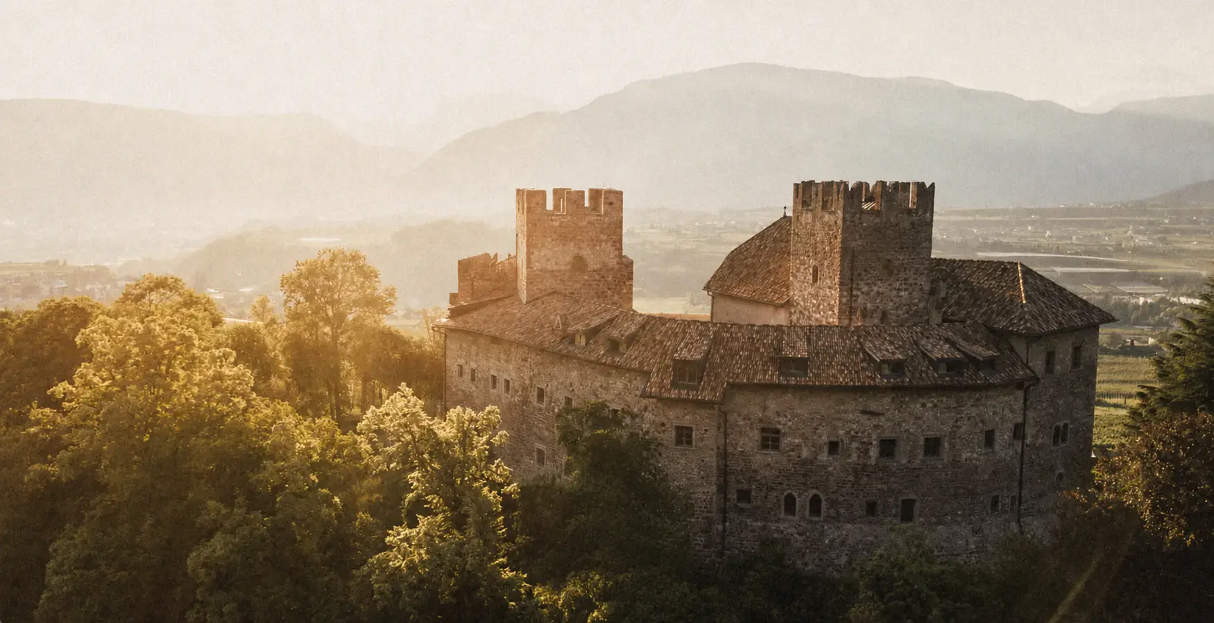 Historic castle on a wooded hillside at sunset.