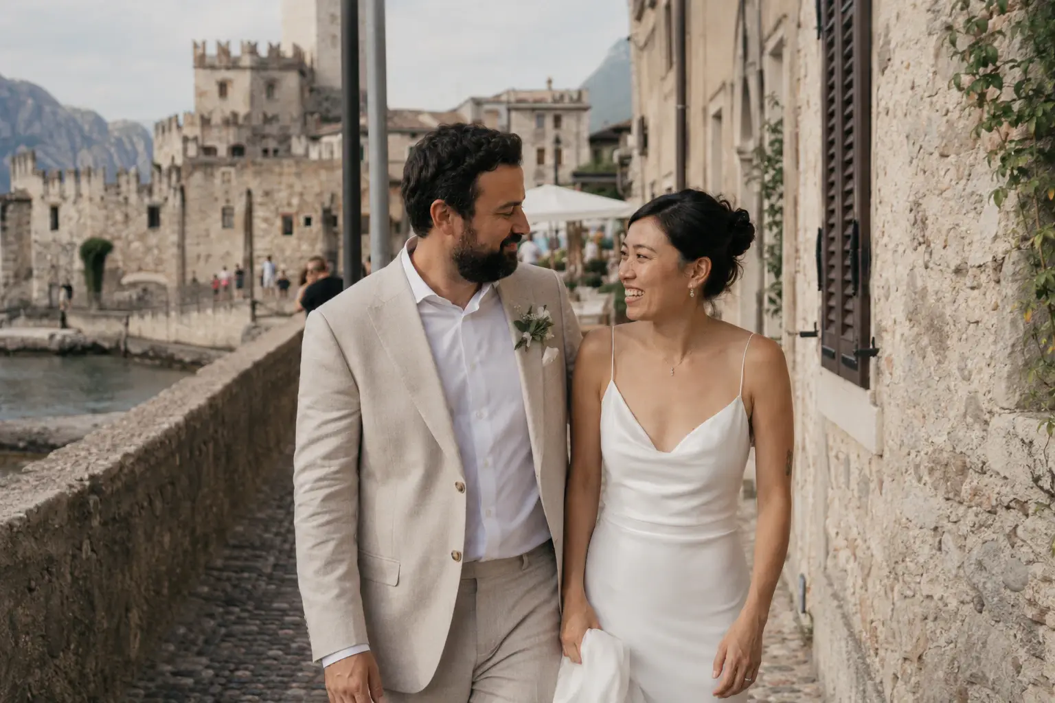 Couple walking beside historic stone buildings in Malcesine.