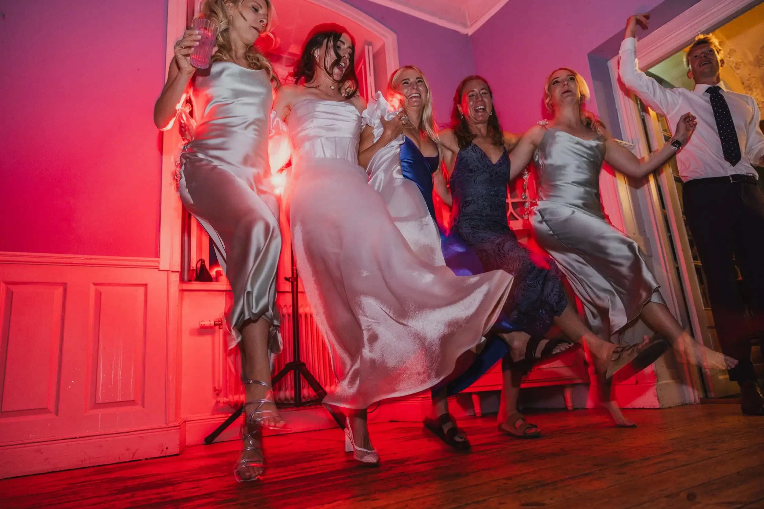 Group of women dancing and celebrating at a party with red lighting.
