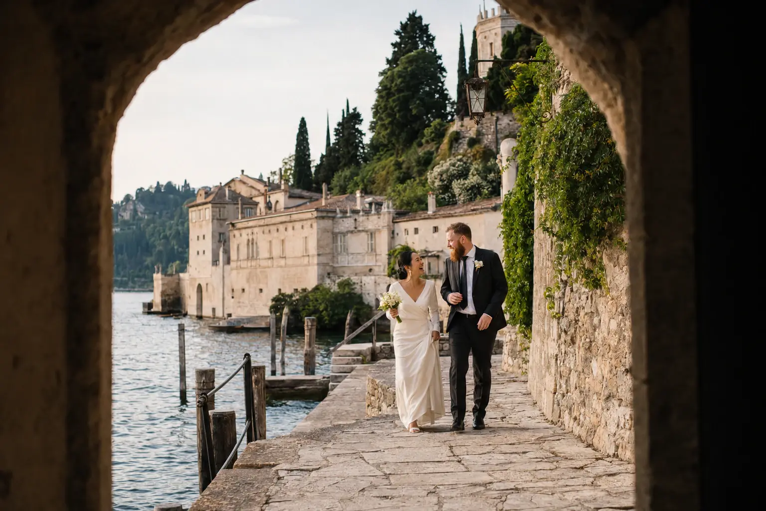 Bride and groom walking through the historic stone archway at Villa San Vigilio on Lake Garda, Italy, during their wedding portraits.