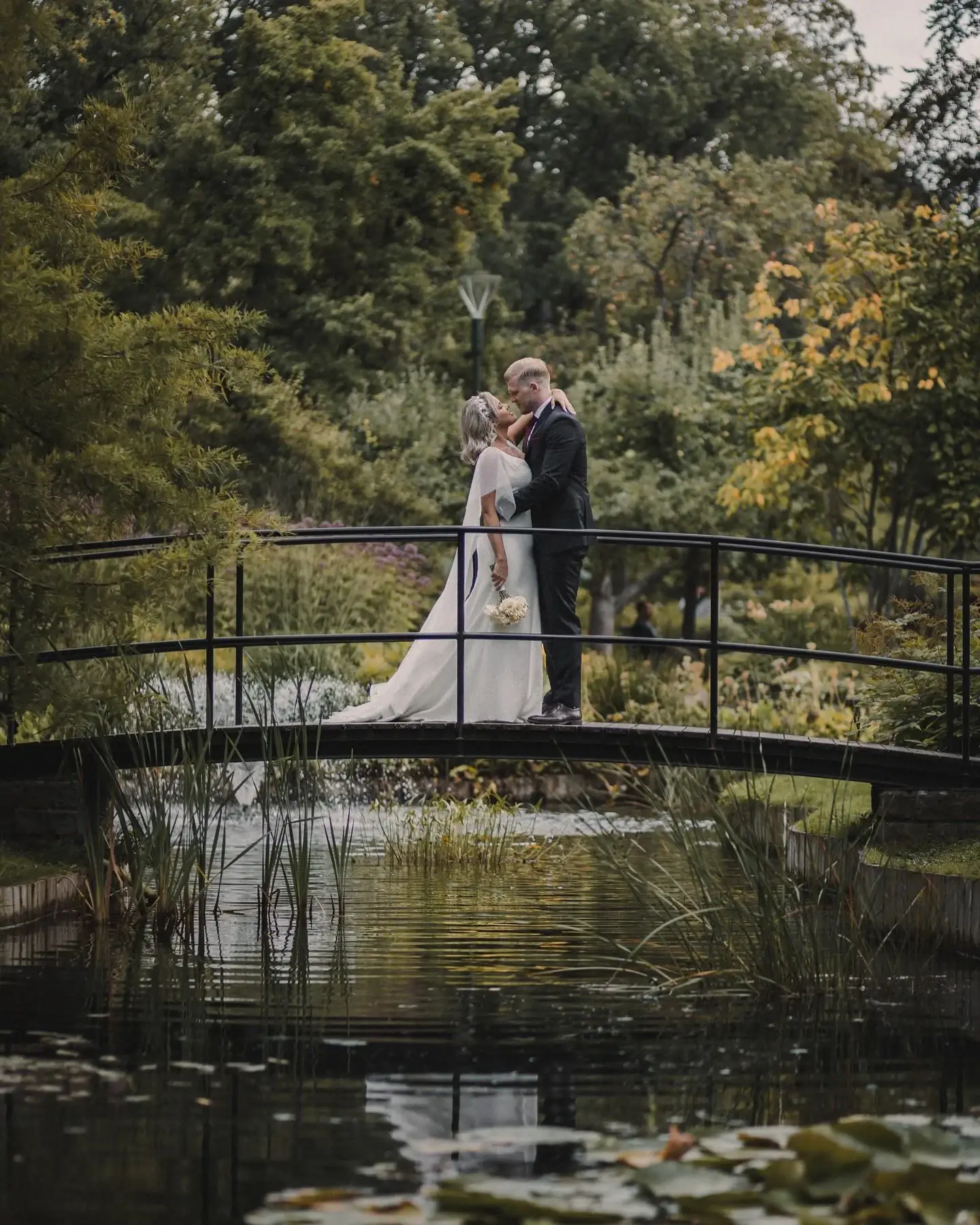 Newlyweds kissing on a garden bridge.